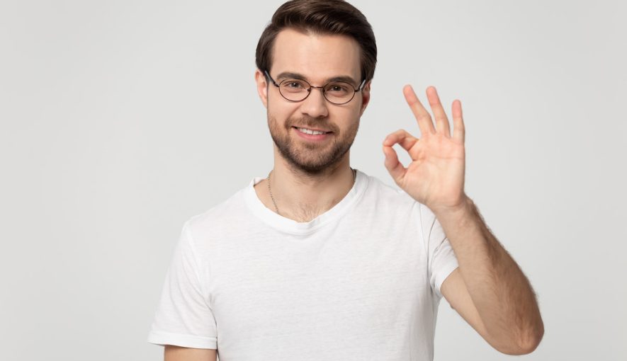 Head shot portrait young happy guy in eyewear showing okay gesture, isolated on grey white studio background. Millennial smiling male client agrees with promotional propose, accepting good offer.